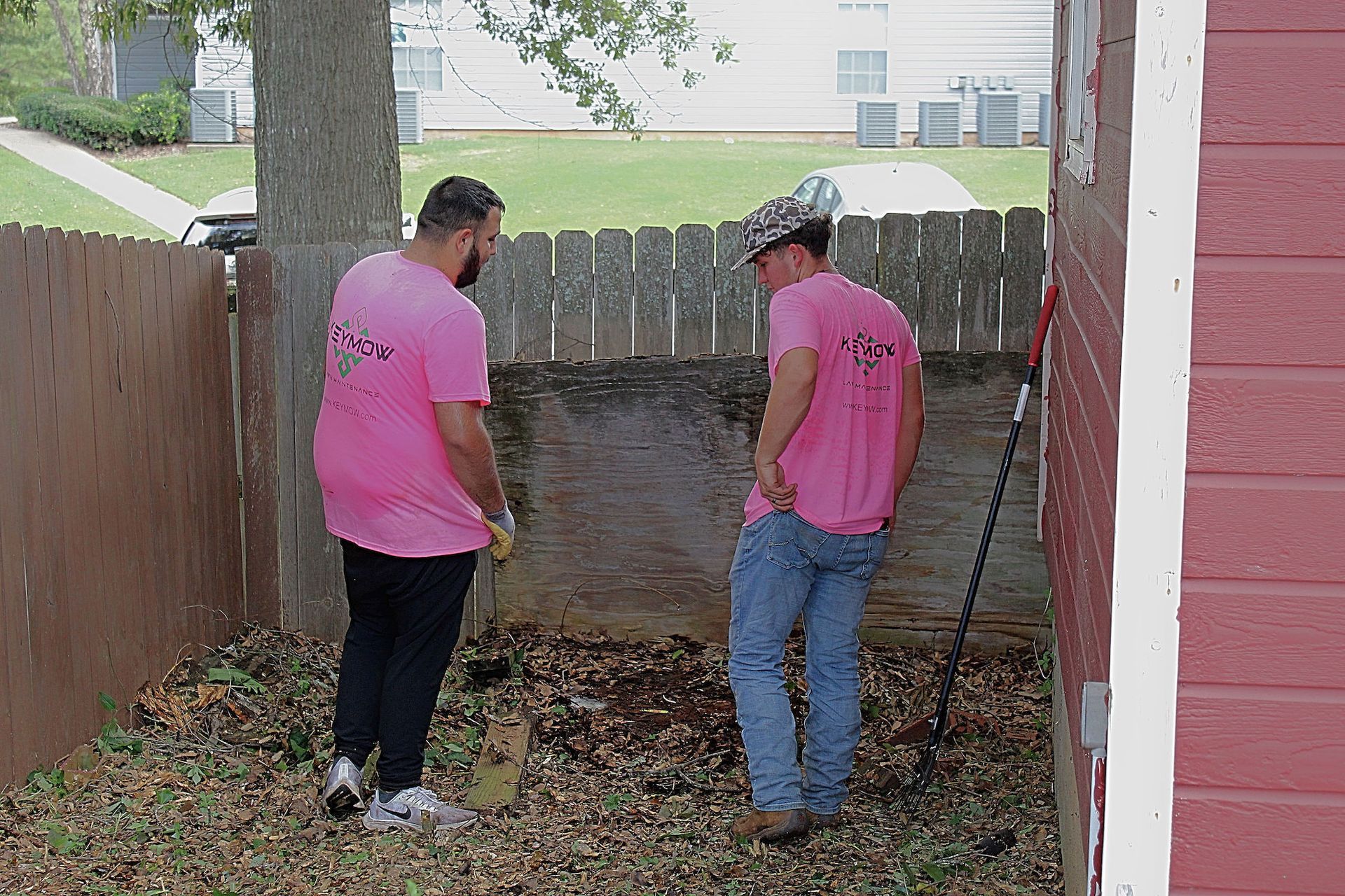 Two people in pink shirts standing by a wooden fence, looking at a large hole in the ground.