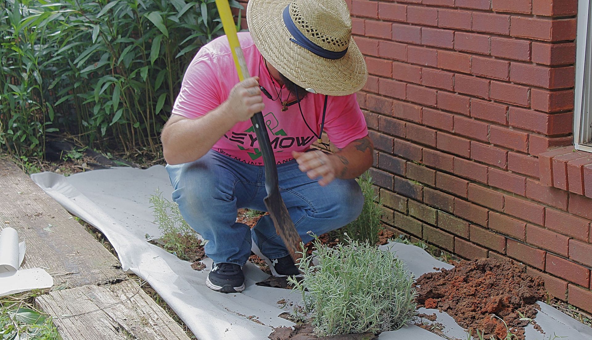 Person crouching beside a brick wall, planting or tending small flowers in a garden bed.