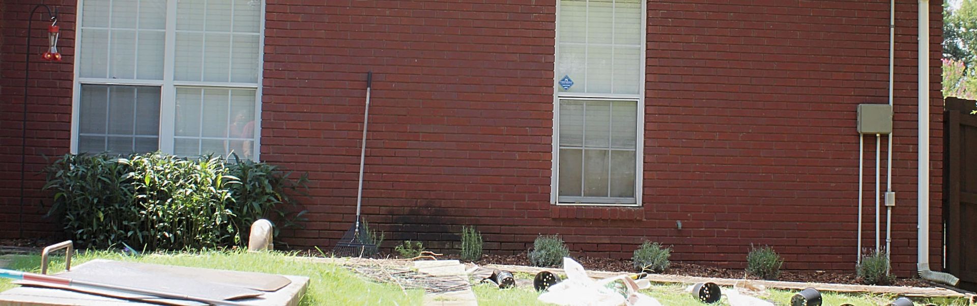 Brick building exterior with windows, shrubs, and a concrete walkway in front