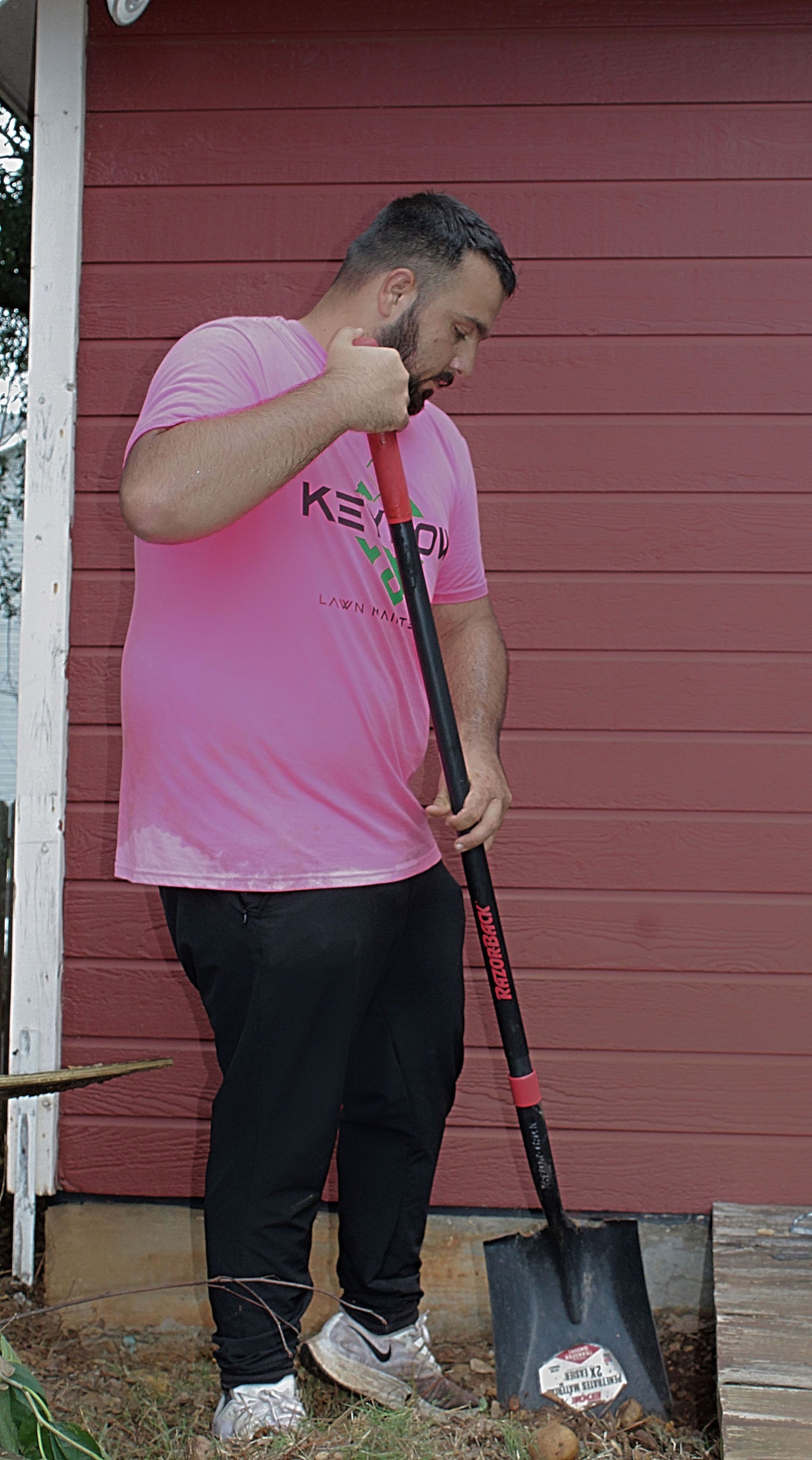 Person in a pink shirt using a shovel beside a red building.