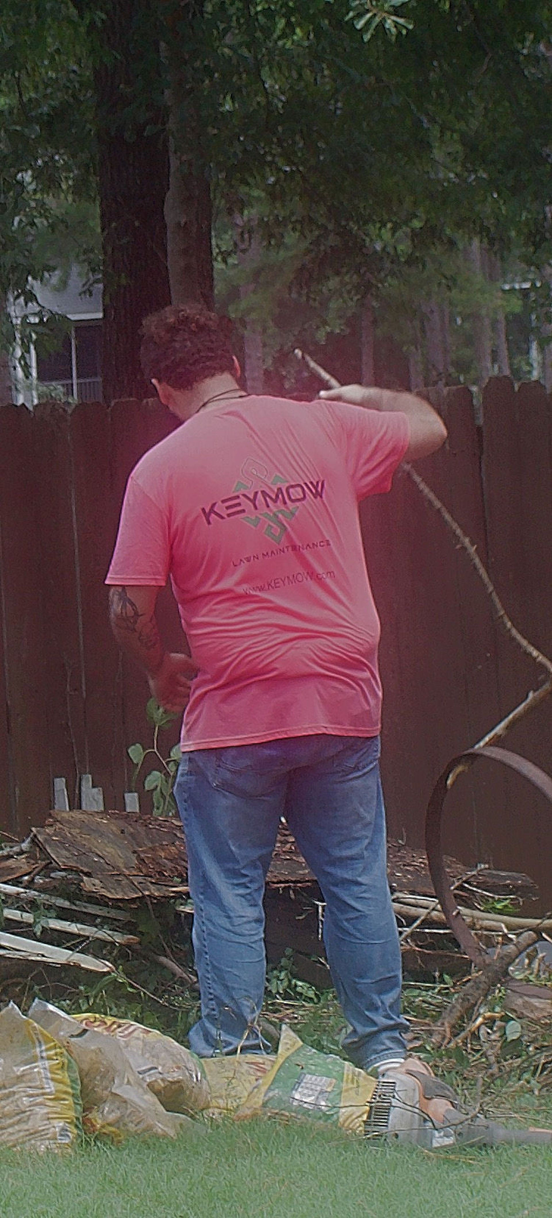 Person in a pink shirt and jeans standing outdoors near a tree, holding a hose or rope.