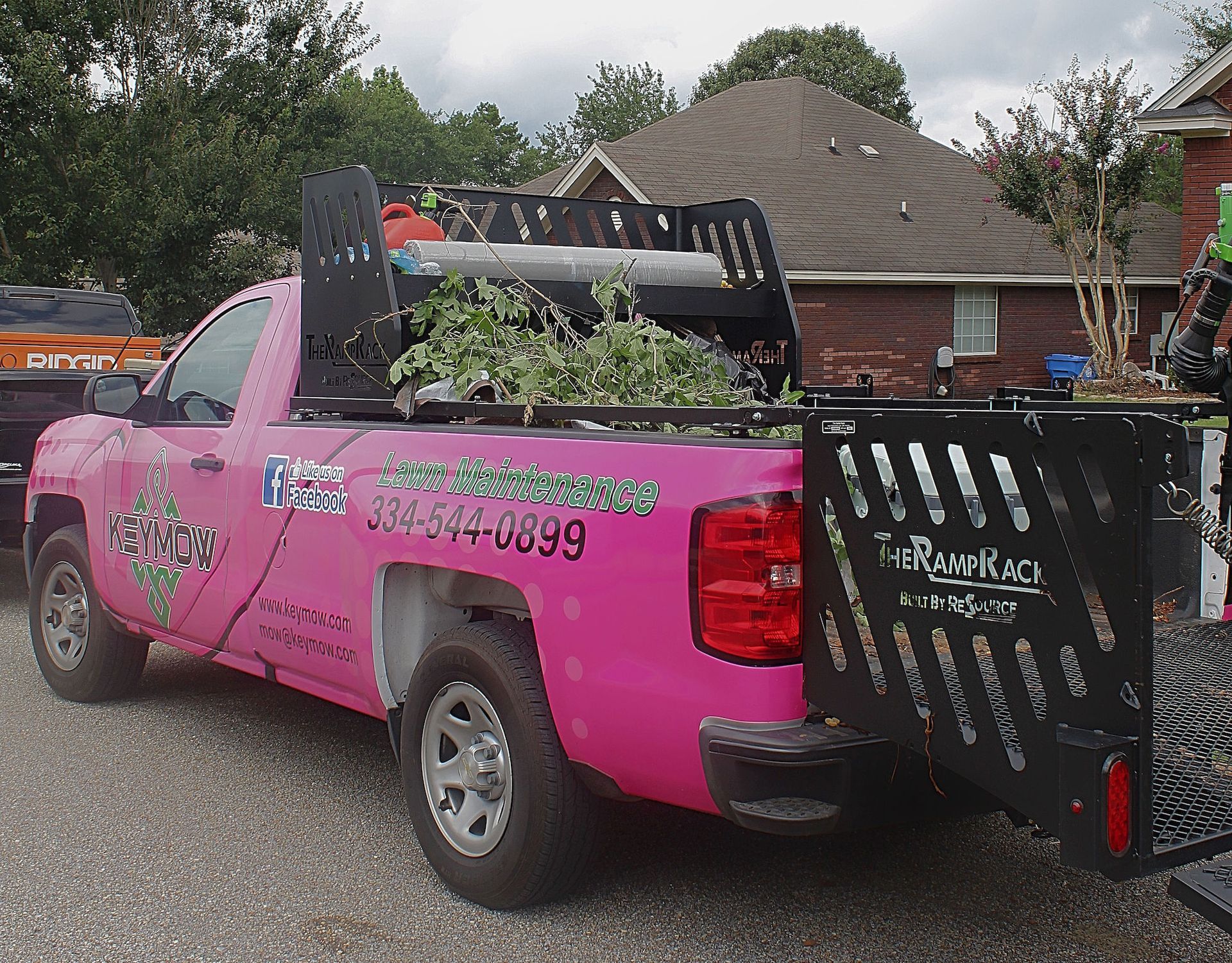 Pink pickup truck with a large black rear gate, parked on a gravel drive beside a house.