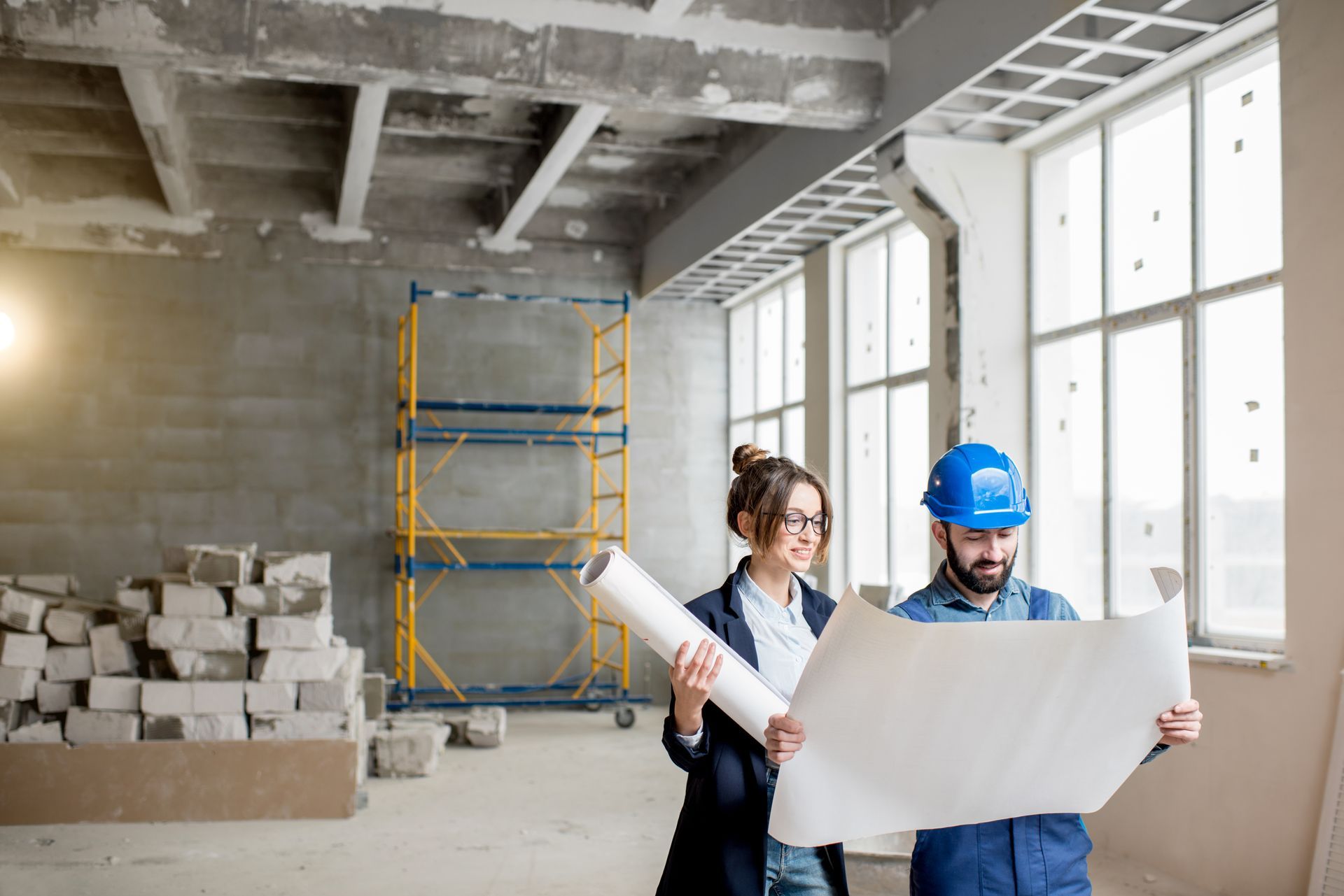 A man and a woman are looking at a blueprint in a building under construction.