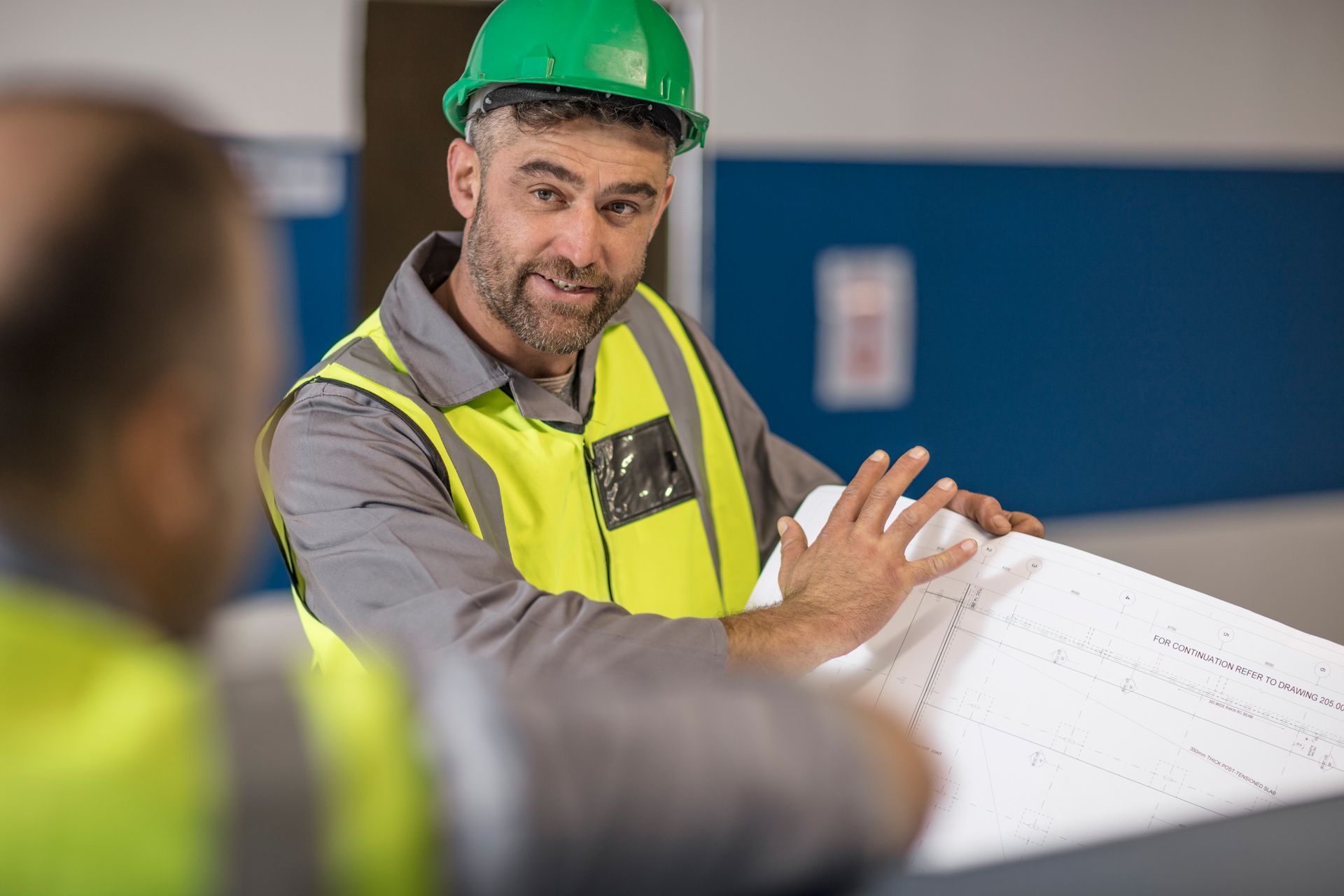 A man wearing a hard hat and safety vest is looking at a blueprint.