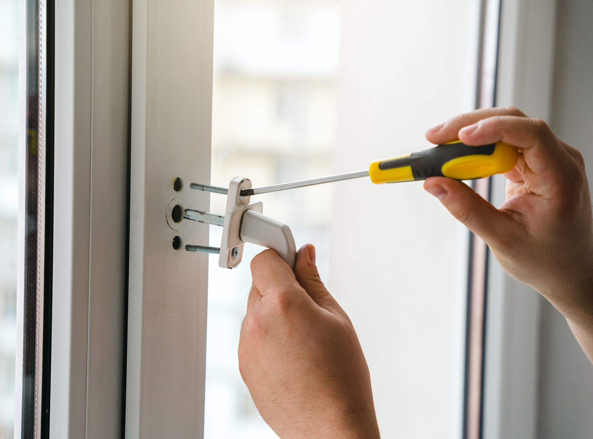 A person is installing a window handle with a screwdriver.