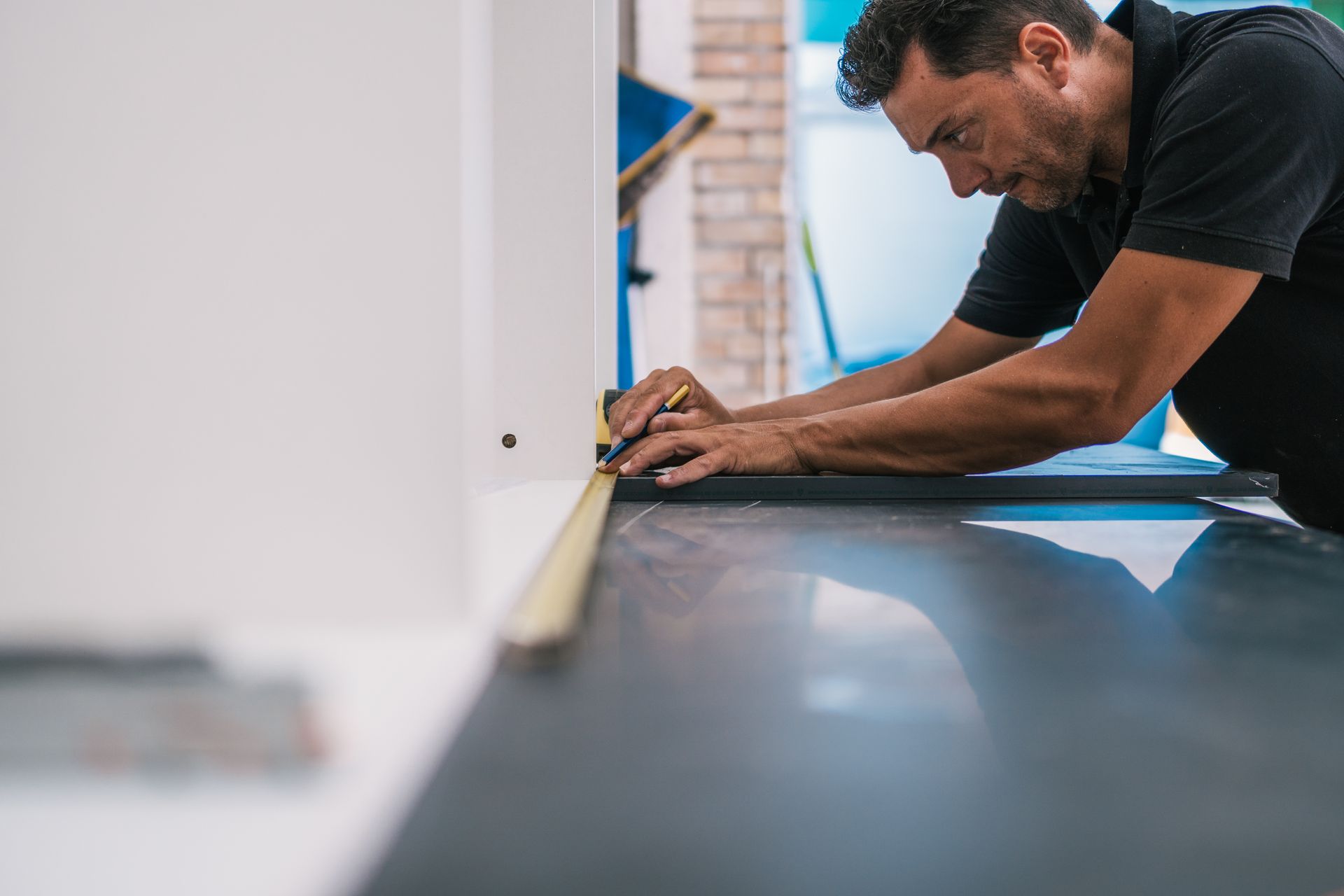 A man is measuring a piece of wood with a tape measure.