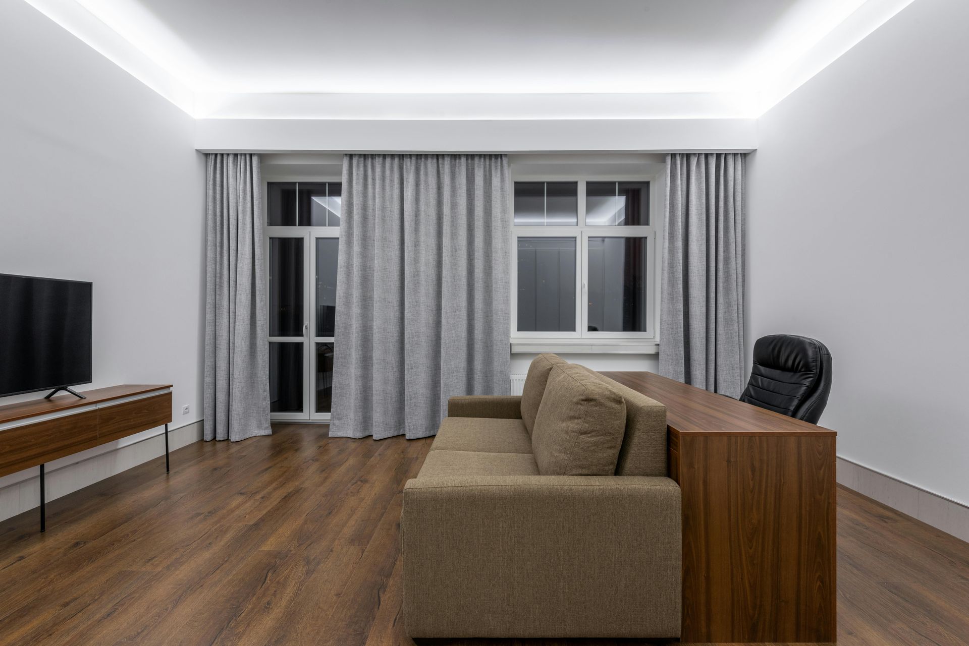 Modern living room with brown sofa, wooden desk, and TV on laminated floors