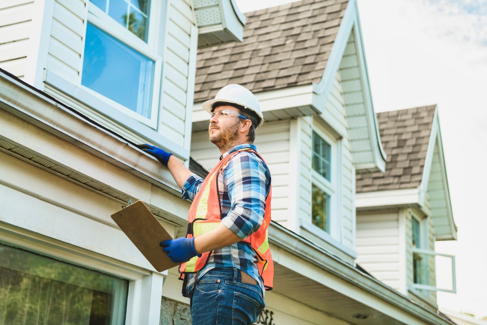 A man is standing in front of a house holding a clipboard.