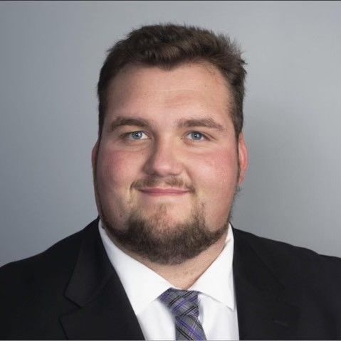 Adam Wolfe with a beard is wearing a suit and tie.