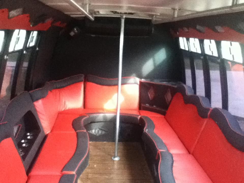 Red-and-black leather lounge seating inside a small cabin or party bus with a central pole and wood floor.