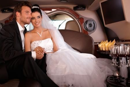 Bride and groom seated in a luxury car, smiling and holding hands in formal wedding attire