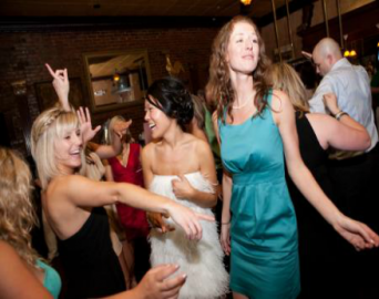 People dancing at a lively party, with two women in bright dresses in the foreground.