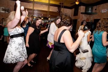 Guests dancing at a crowded indoor party, with one woman in a black dress in the foreground.