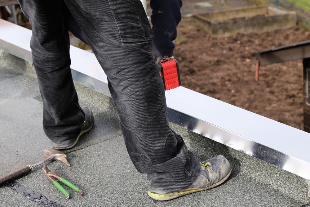 A Man Is Standing on A Roof with A Hammer and Pliers — Fraser Coast Waterproofing in Craignish, QLD