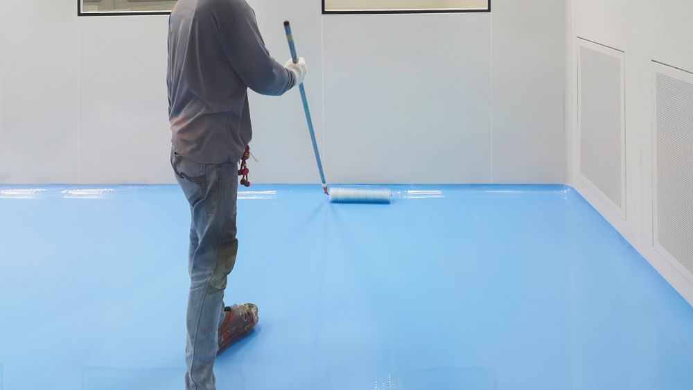A Man Is Painting a Blue Floor with A Mop — Fraser Coast Waterproofing in Craignish, QLD