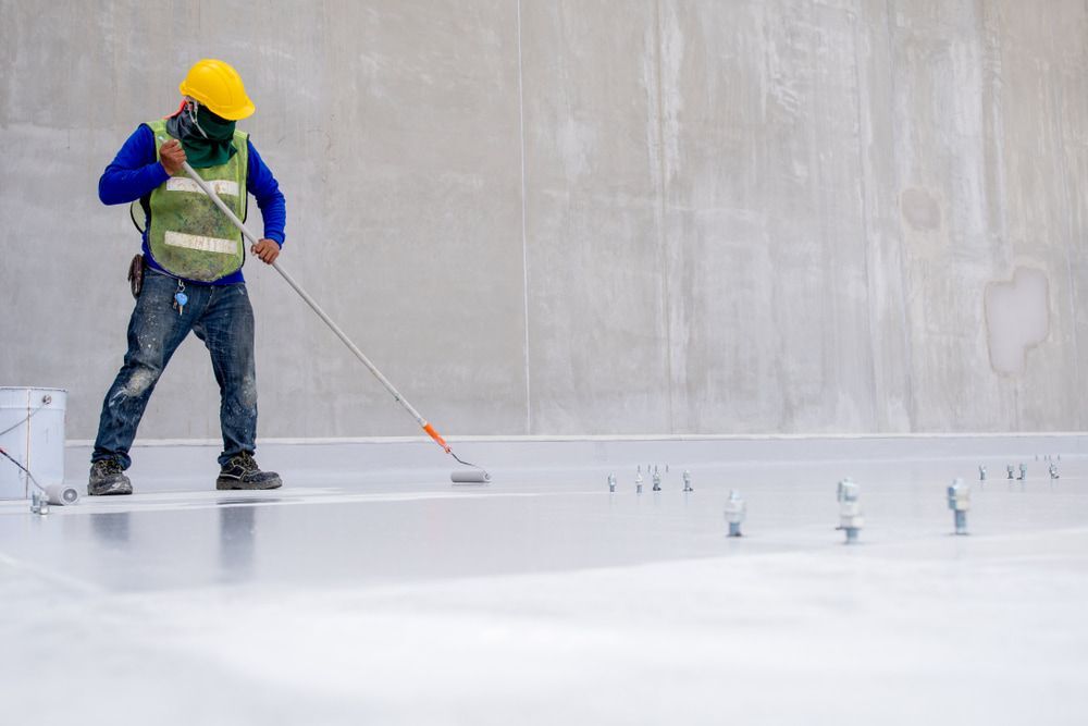 A construction worker is painting a concrete floor with a roller — Fraser Coast Waterproofing in Eli Waters, QLD