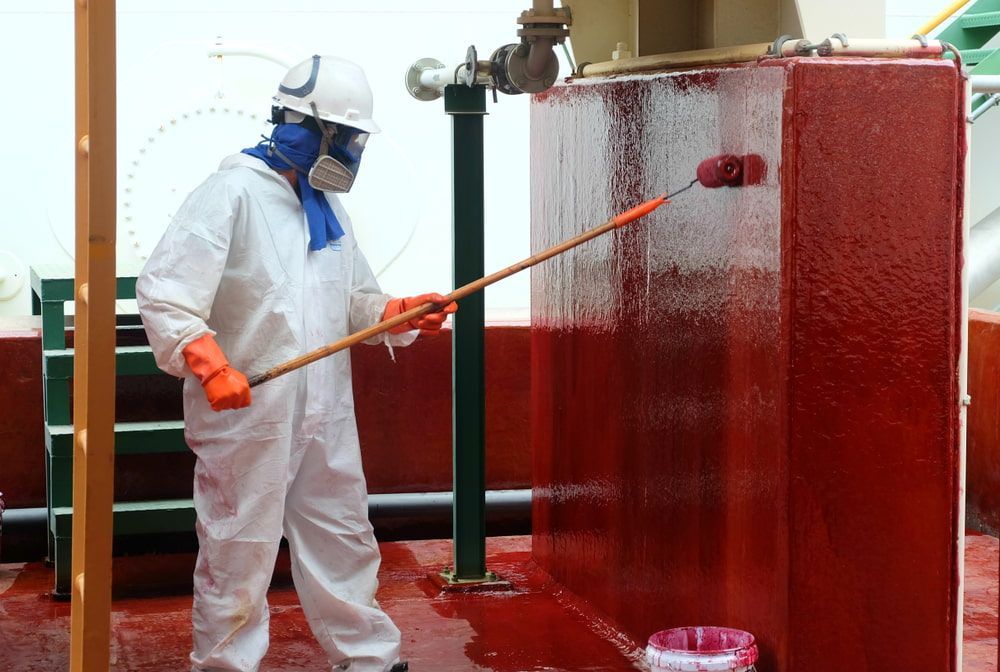 A Man in A Protective Suit Is Painting a Red Wall with A Broom— Fraser Coast Waterproofing in Eli Waters, QLD