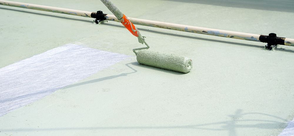 A Person Is Painting a Roof with A Paint Roller — Fraser Coast Waterproofing in Craignish, QLD