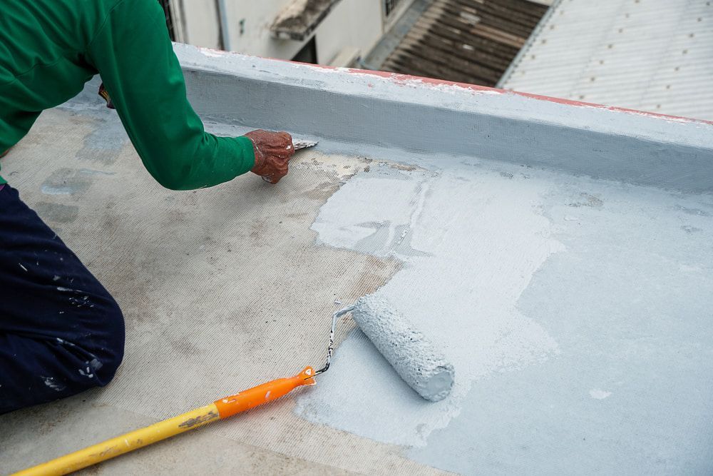 A Man Is Painting a Roof with A Roller — Fraser Coast Waterproofing in Point Vernon, QLD