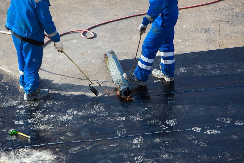 Two Men in Blue Jumpsuits Are Working on A Roof — Fraser Coast Waterproofing in Pialba, QLD