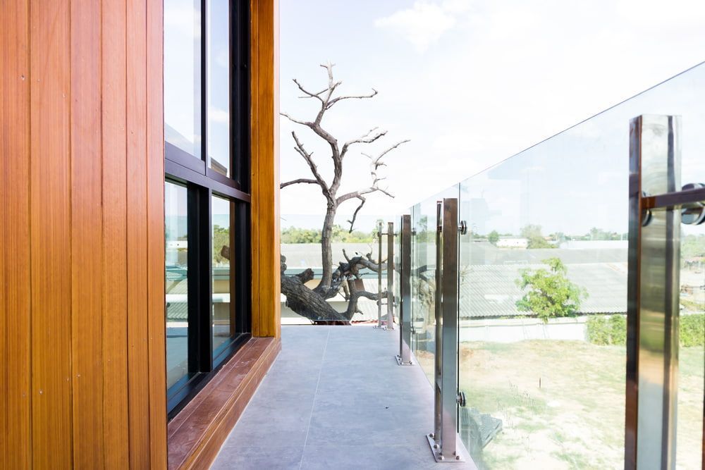 A Balcony with A Glass Railing and A Tree in The Background — Fraser Coast Waterproofing in Urangan, QLD