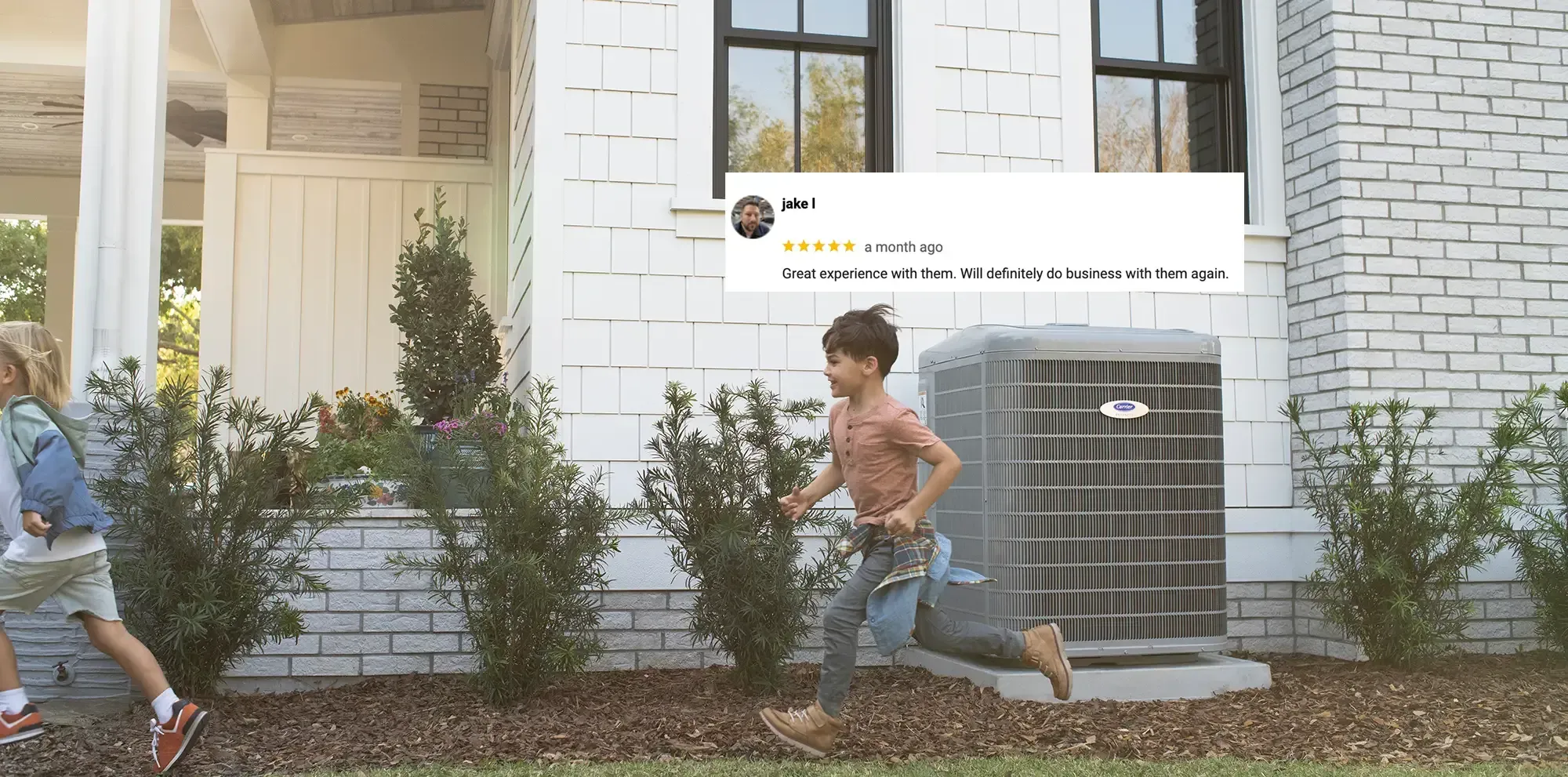 Two children running past a white brick house with shrubs and a window air conditioner