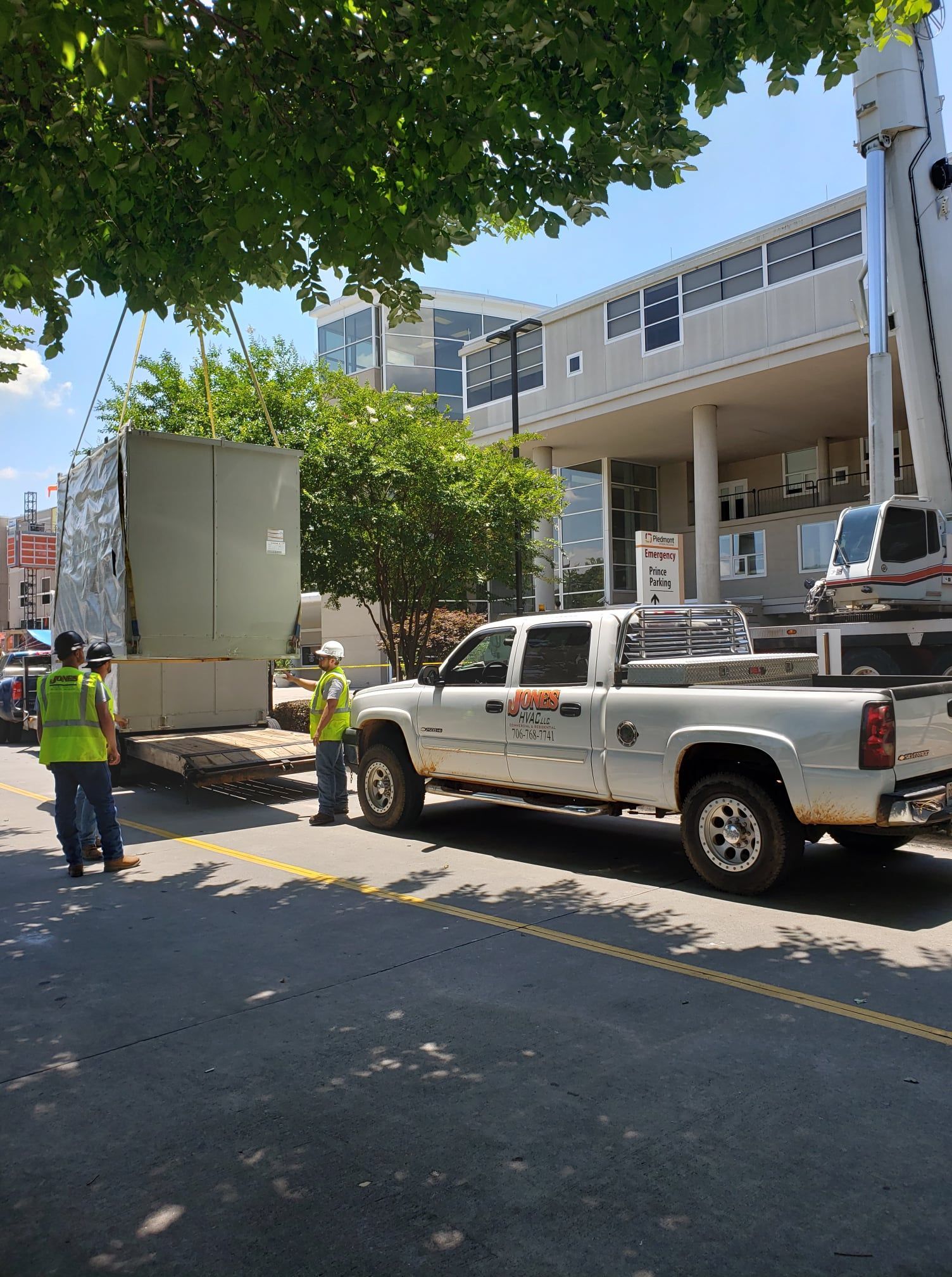 Workers in safety vests unload a large container from a flatbed truck on a city street.