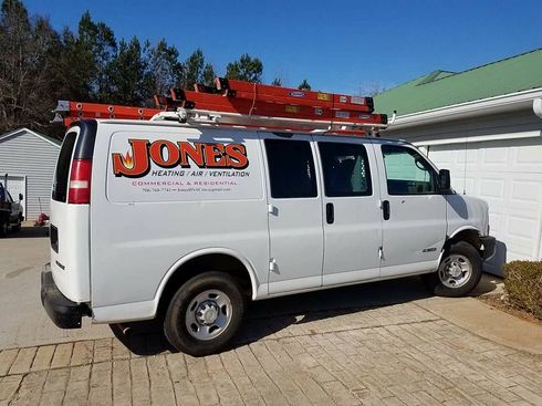 White Jones service van with red ladders parked beside a garage in a driveway