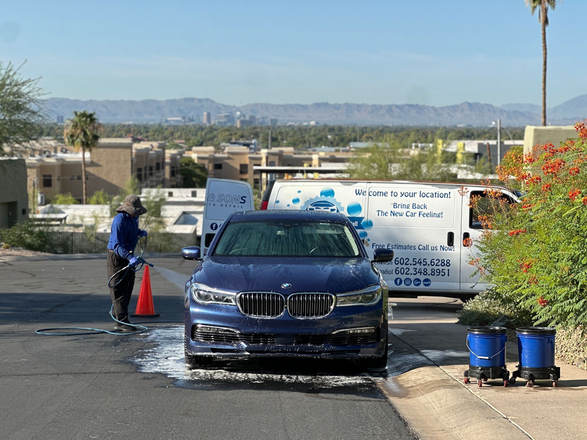 A person in a blue uniform and gloves uses an extraction tool to deep clean a textured black and gray car seat.
