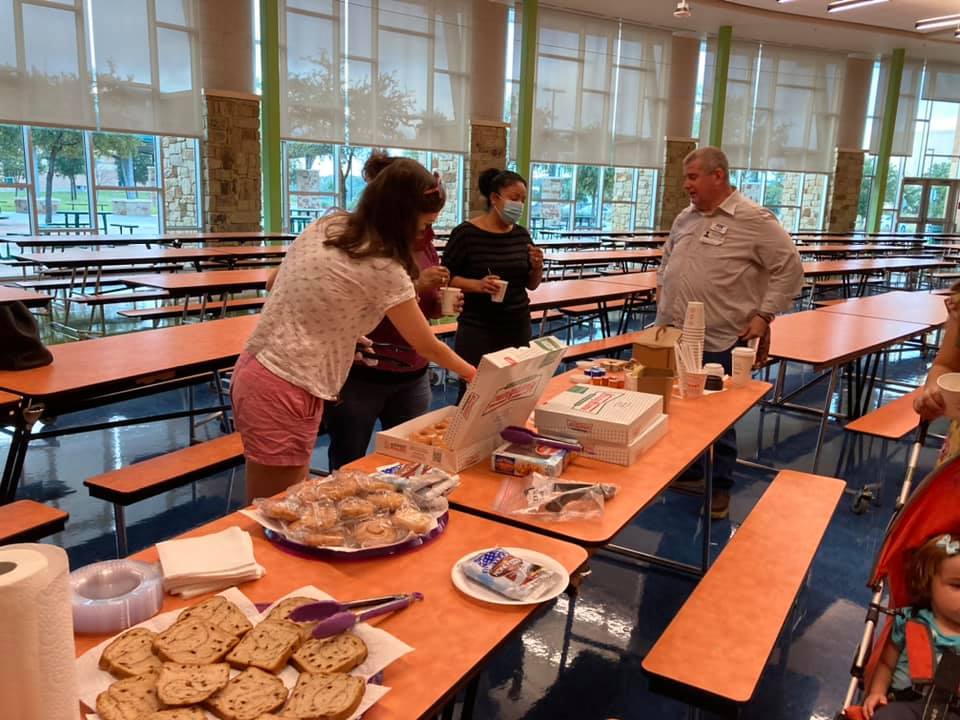 People serving food on cafeteria tables in a bright, empty dining hall