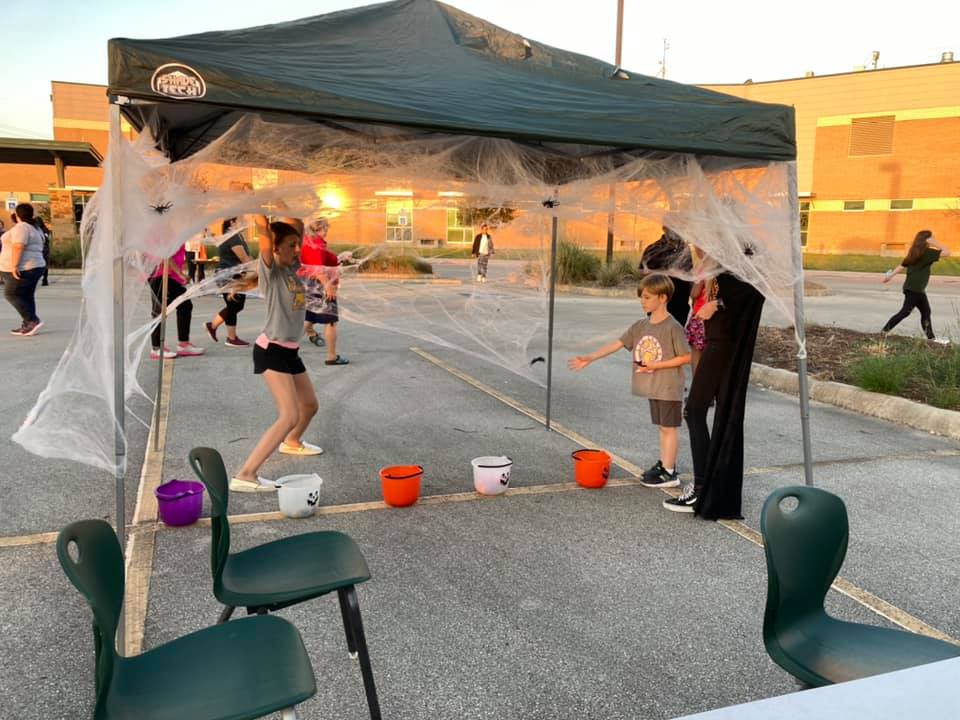 Children under a tent with Halloween cobwebs, using a small play setup in a parking lot at dusk