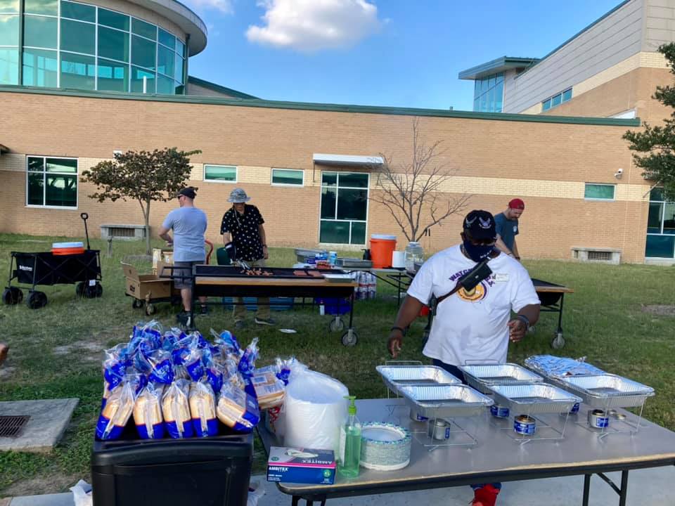 Outdoor food service setup on campus with people arranging trays and bread tables near a building