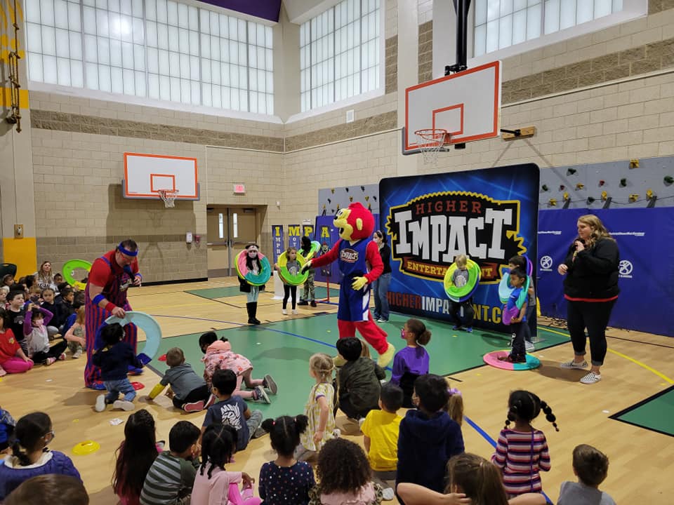 Costumed performers at a gym event with children watching near basketball hoops and a “THOR IMPACT” banner.
