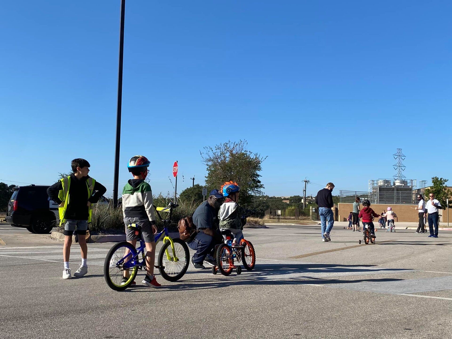 Children with bicycles on a paved plaza, with a person in the background and clear blue sky