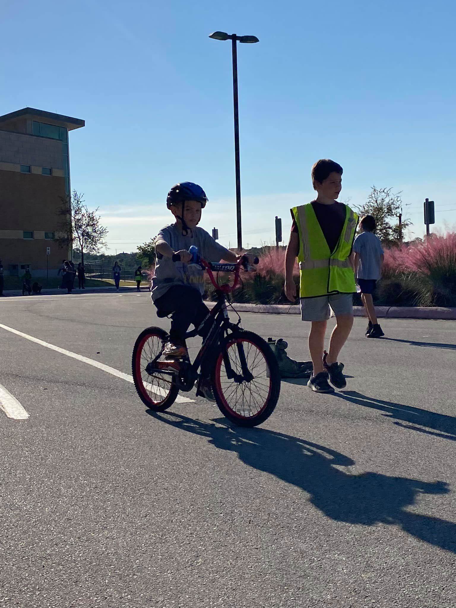 Child on a bicycle with another child walking nearby on a sunny paved path.