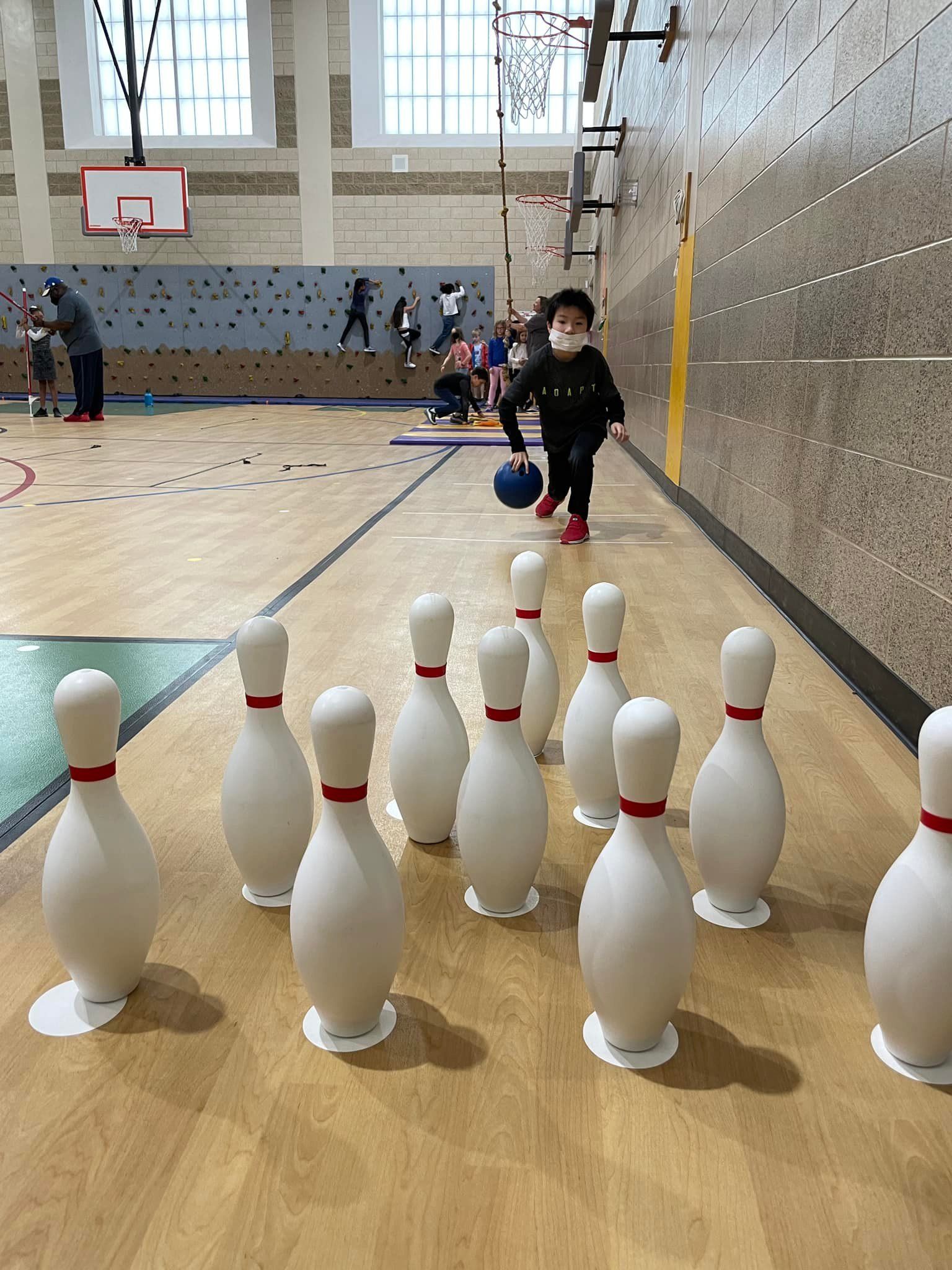 Bowling alley with toy pins lined up in the foreground and a child rolling a ball toward them.