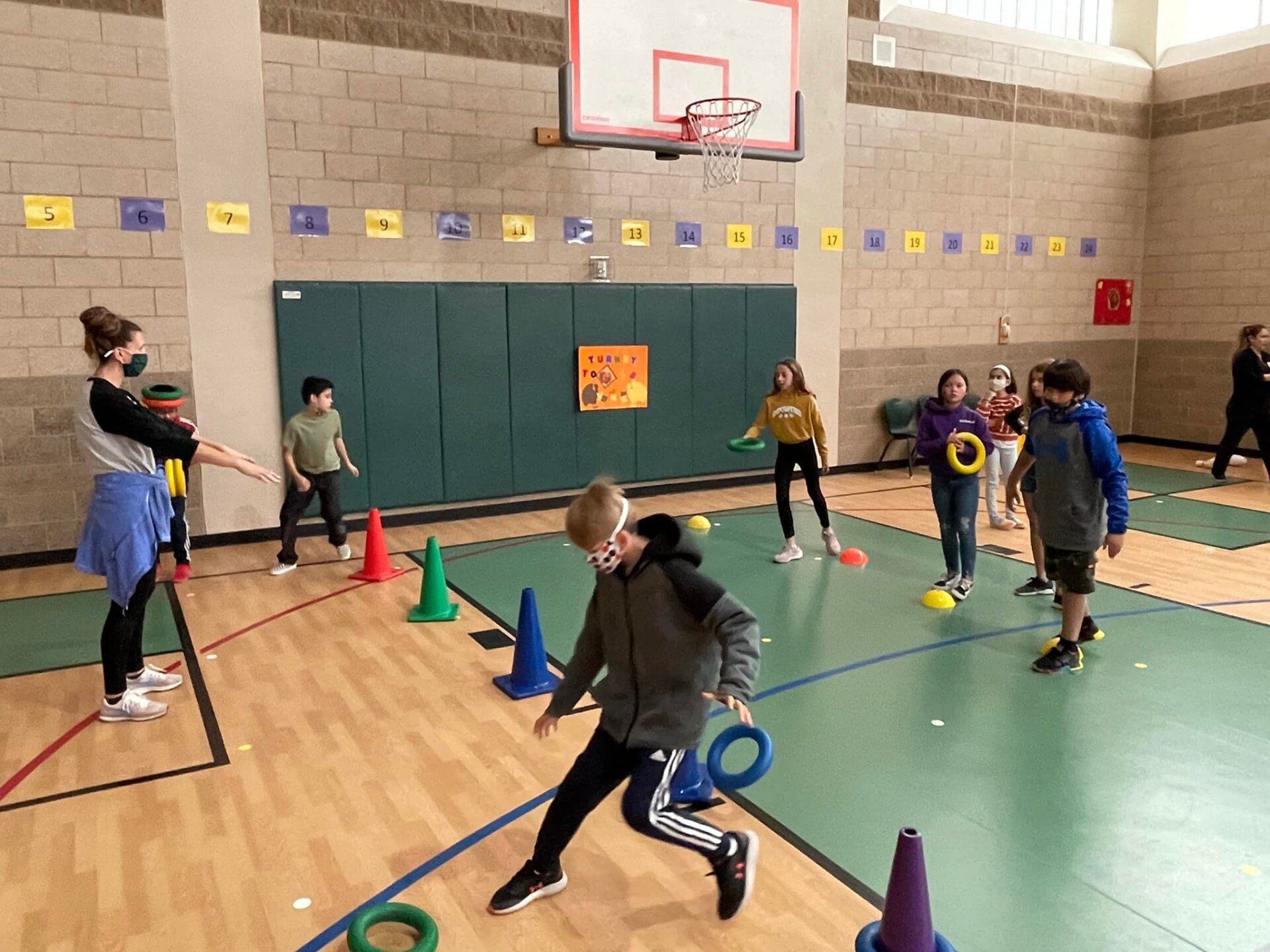Children playing an indoor obstacle course in a gym, weaving around colorful cones with bats and hoops