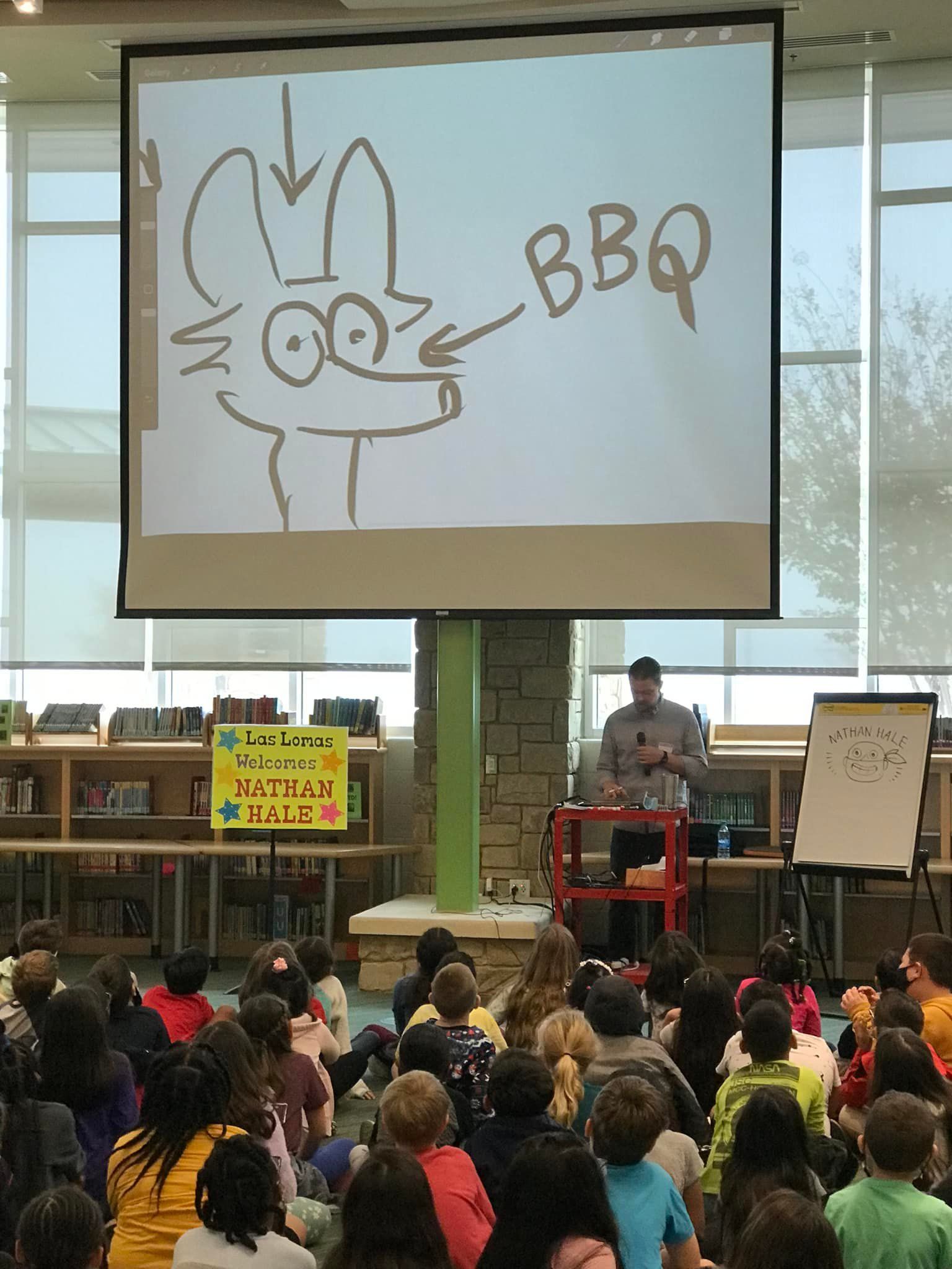 Presenter drawing on large screen to an audience, with a cartoon cat and the word “BBQ” displayed.