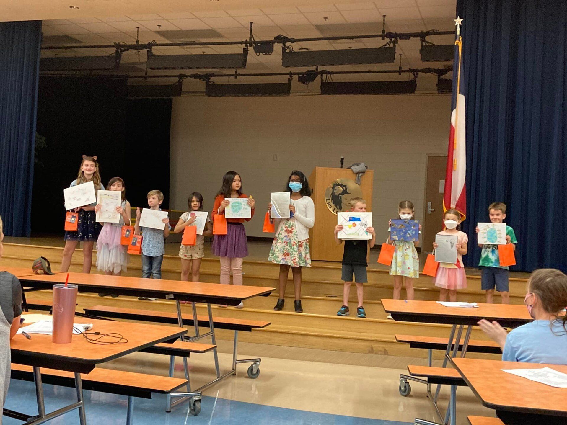 Children standing on a stage, holding drawings during a school presentation