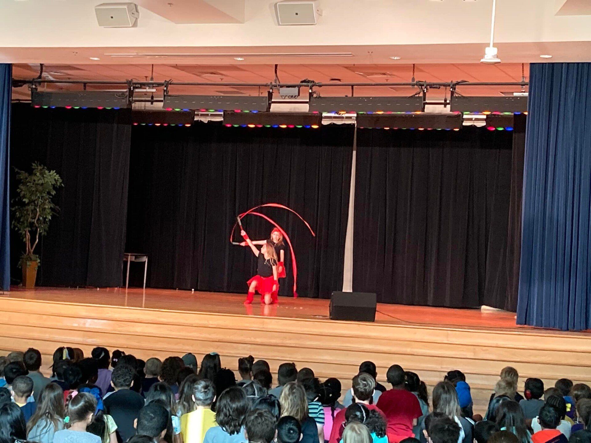 Dancer in red costume performs with ribbon hoops on a stage before an audience