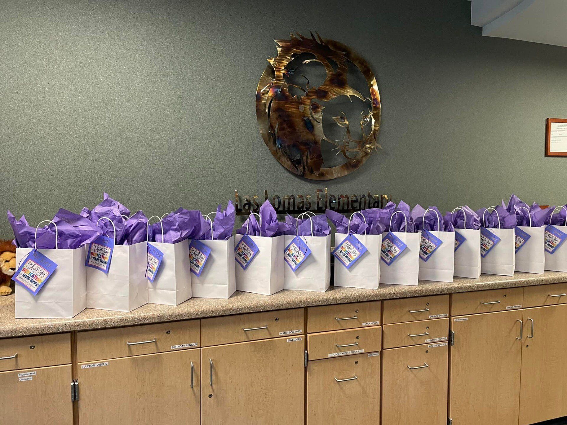 Rows of purple gift bags with white tags lined on a counter beneath a wall wreath.