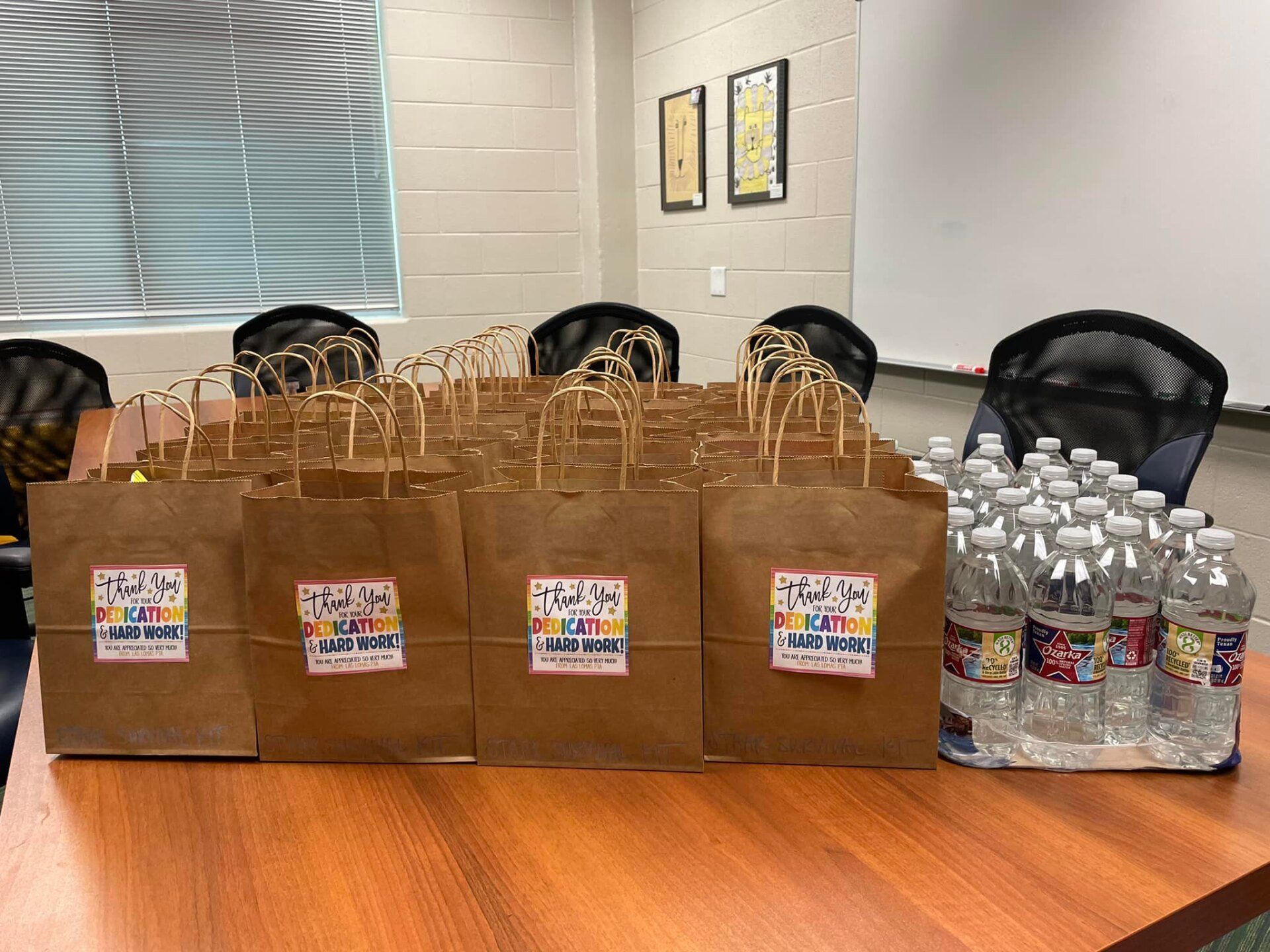Paper bags of supplies and water bottles lined up on a conference room table.