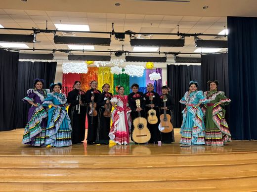 Mariachi band in black suits with colorful folkloric dancers on a stage with a black curtain backdrop
