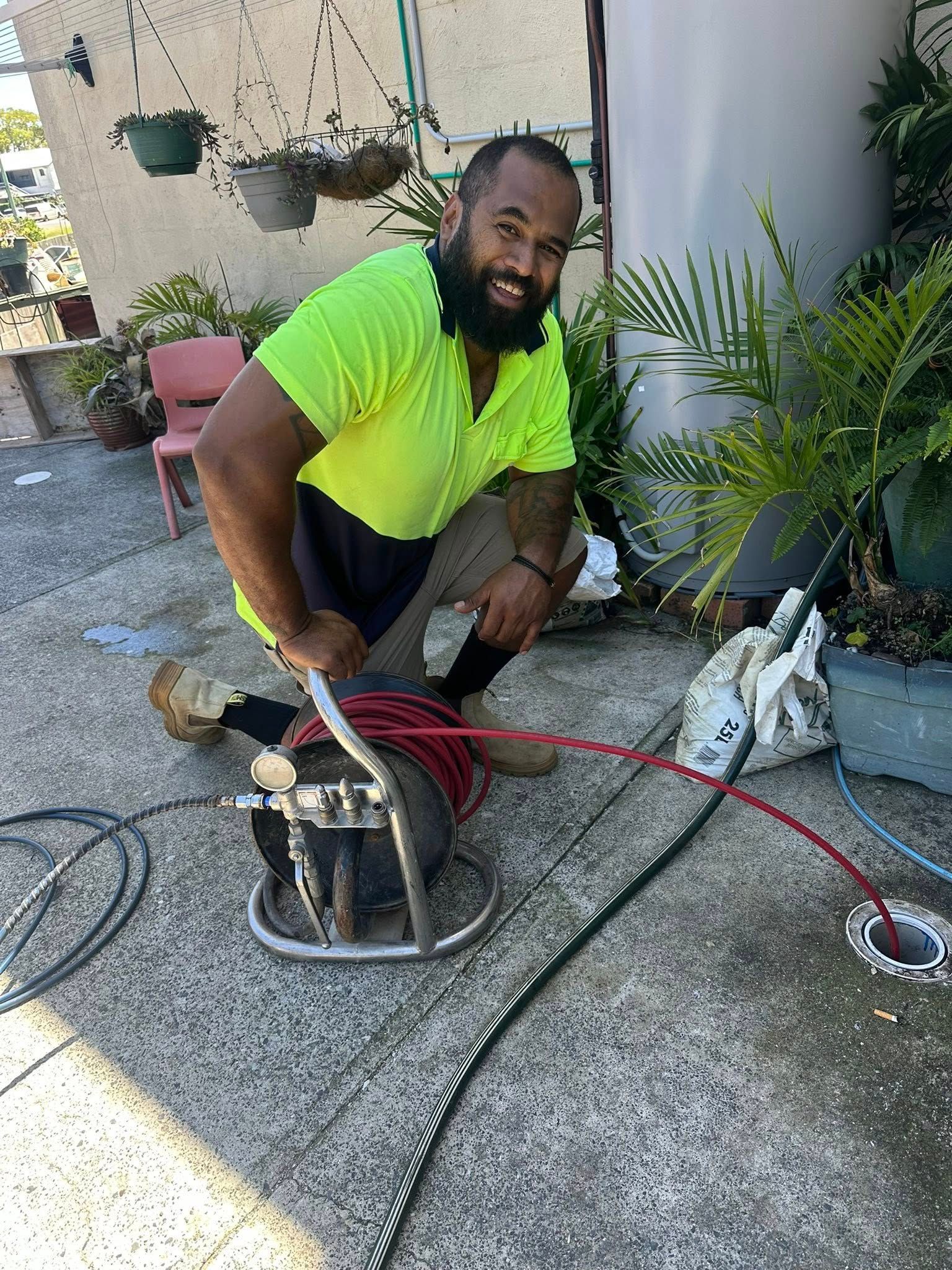 Worker Kneeling with A Red Hose and Equipment on A Concrete Patio — Chris Murphy Plumbing and Maintenance in Langley Vale, NSW