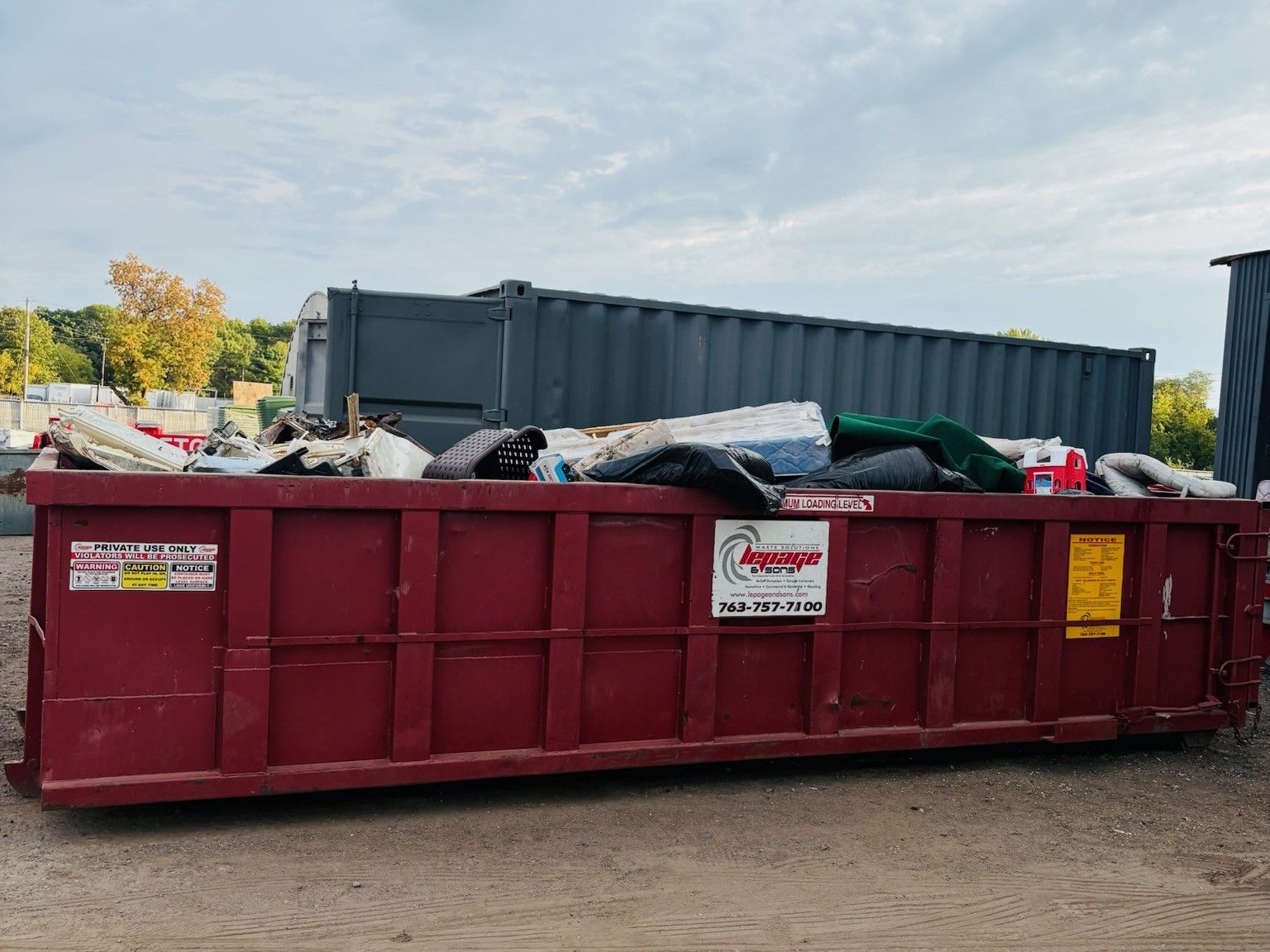 A roll-off dumpster from LePage & Sons is filled with trash.