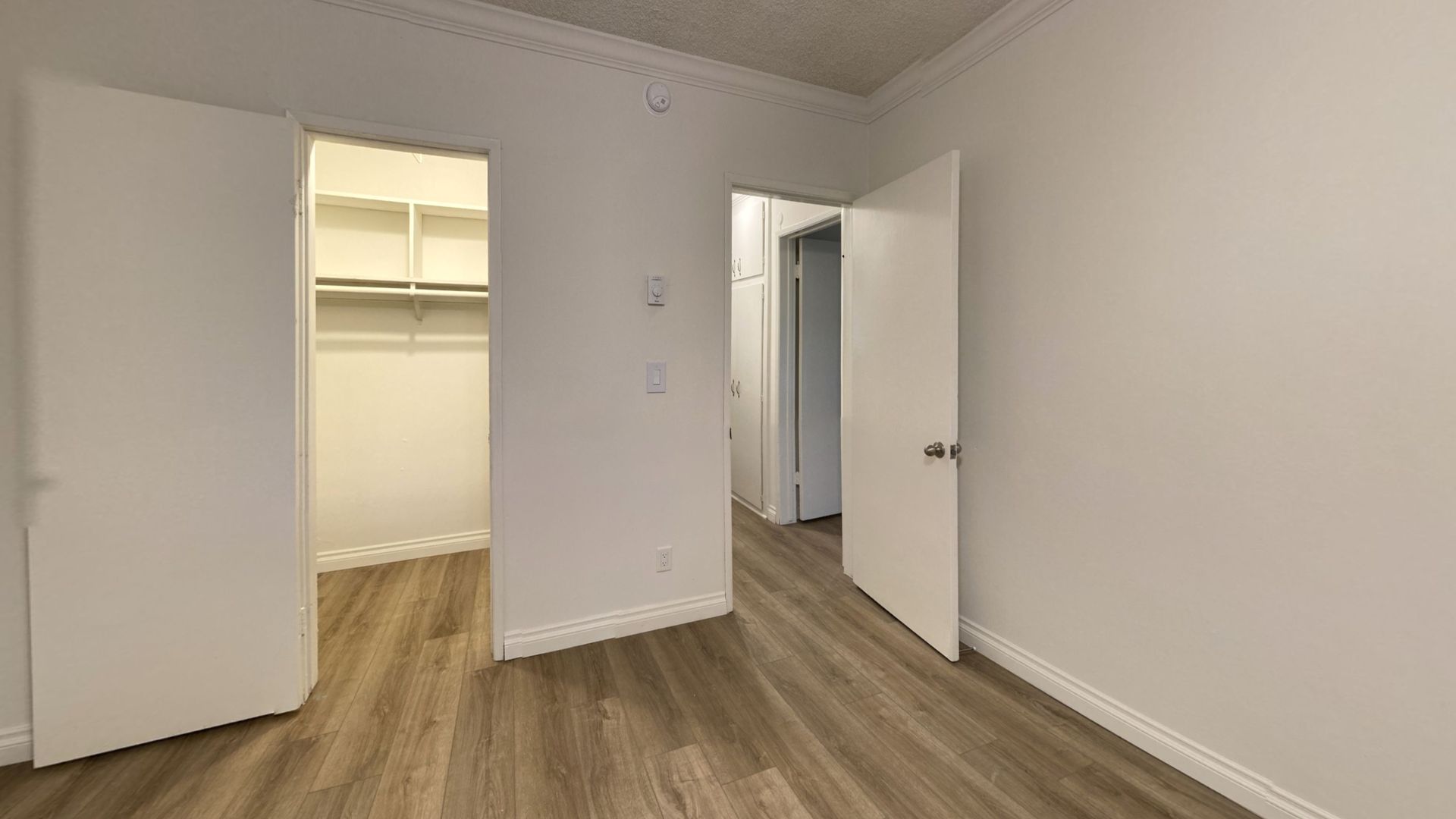 Empty room with two open doors: closet and doorway to another room; light wood floors, white walls.