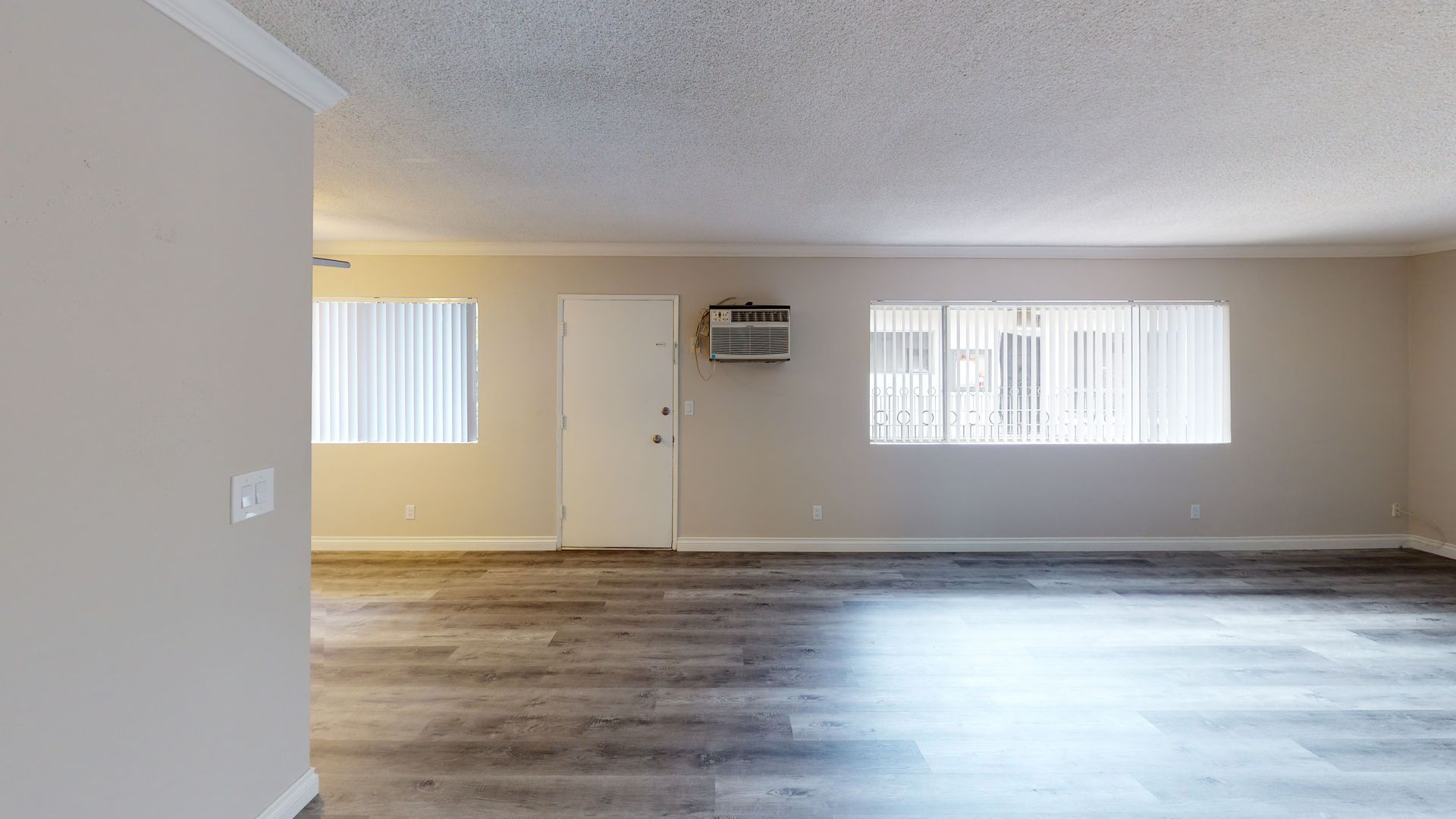 Empty apartment interior with neutral walls, light wood flooring, and windows.
