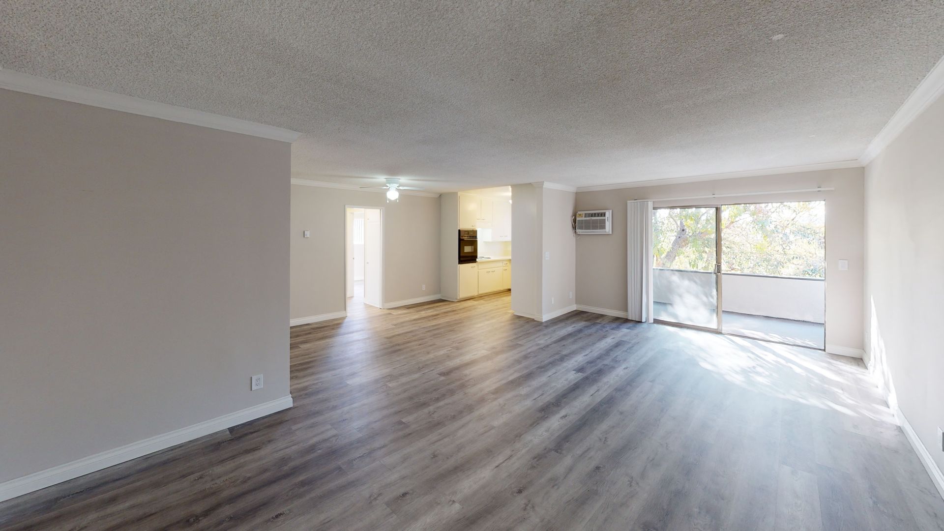 Spacious, empty apartment interior with grey wood floors, white walls, and a balcony with natural light.