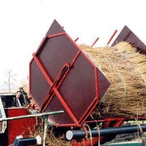Rietmaaimachine die een lading riet van een vrachtwagen laadt. Rood frame, bruin paneel, buitenopstelling.