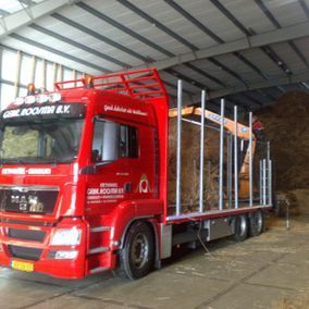 Een rode vrachtwagen laadt rietbalen in een loods.